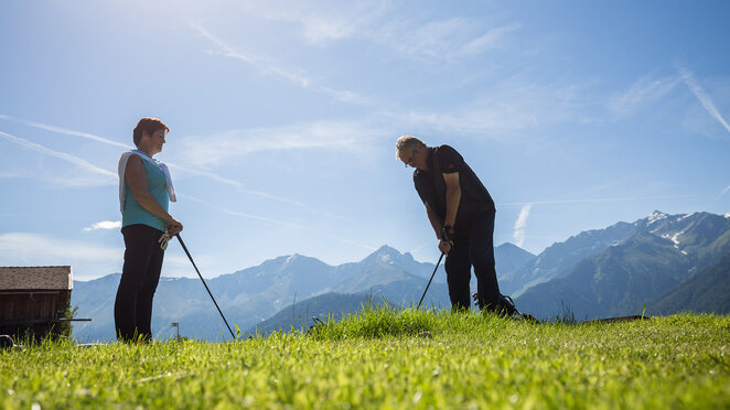 Golfer schlägt einen Ball auf der Driving Range vor Bergkulisse